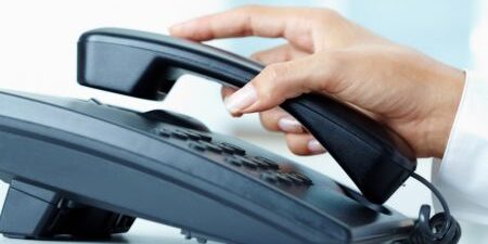 Female hand holding phone receiver over telepnone